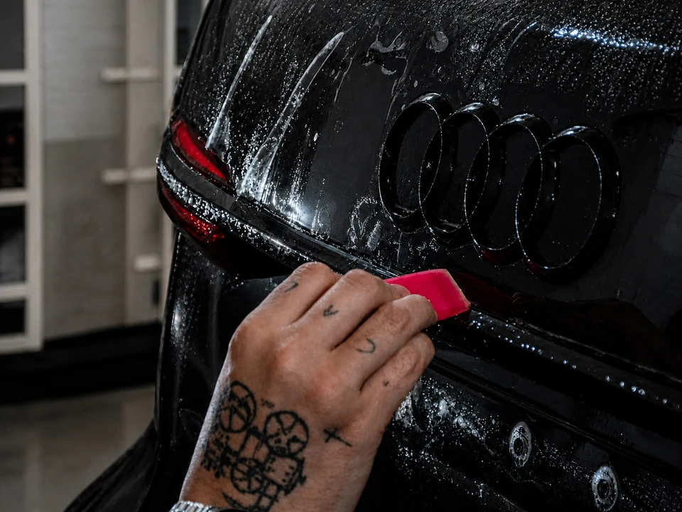 Technicien en atelier applique à la main un film PPF (Paint Protection Film) transparent sur le capot d'une Porsche 911 jaune Racing